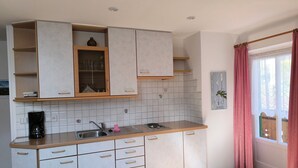 Een kleine keuken met witte kastjes, een koffiezetapparaat en een wastafel.
