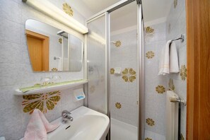 Une salle de bain équipée d’une douche, d’un lavabo, d’un miroir et de carreaux décoratifs.