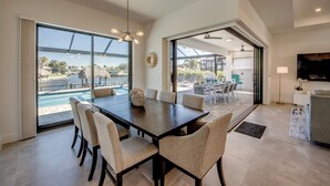 A spacious dining area with a large table and chairs, large windows offering a view of a pool and outdoor seating. - Villa Happy Place - on water, pool, spa, views, boating (Cape Coral)