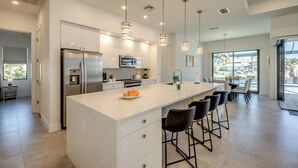 A modern kitchen with a large island, stainless steel appliances, pendant lighting, and a view to the outdoors. - Villa Happy Place - on water, pool, spa, views, boating (Cape Coral)