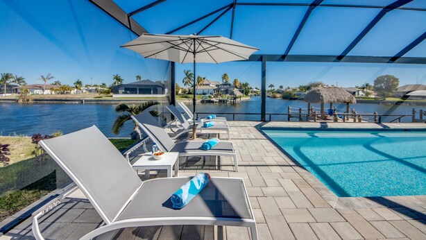 A poolside area with lounge chairs, a covered seating area, and a view of a body of water. - Villa Happy Place - on water, pool, spa, views, boating (Cape Coral)