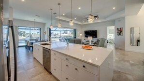 A modern kitchen with a large island, pendant lighting, and a view to the outdoors. - Villa Happy Place - on water, pool, spa, views, boating (Cape Coral)