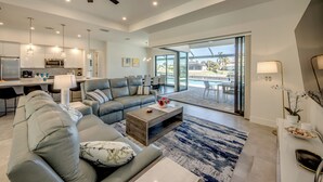 A modern living room with a sectional sofa, a coffee table, and a dining area with chairs. - Villa Happy Place - on water, pool, spa, views, boating (Cape Coral)