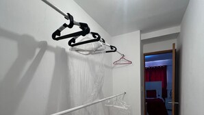 A hallway with a white wall, a ceiling light, a bed with a red curtain, and a door leading to another room. - Penthouse 2BR w/ Private Rooftop Terrace + Views (Santo Domingo)