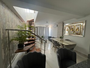 A modern interior with a staircase, dining area, and a wall with framed artwork. - Penthouse 2BR w/ Private Rooftop Terrace + Views (Santo Domingo)