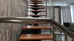 A modern staircase with a geometric wall pattern, metal railings, and a view of a living area with a sofa. - Penthouse 2BR w/ Private Rooftop Terrace + Views (Santo Domingo)