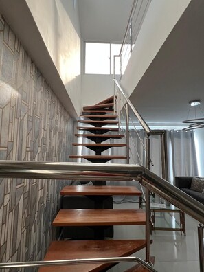 Un escalier moderne, agrémenté d’un motif géométrique sur le mur, de rampes en métal et offrant une vue sur un espace de vie avec un canapé.