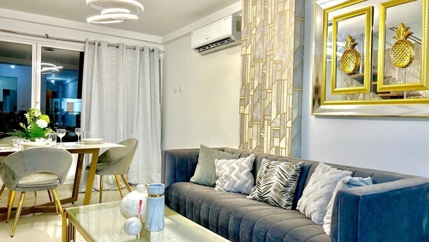 A modern living room with a glass coffee table, grey sofa, and a decorative wall panel. - Penthouse 2BR w/ Private Rooftop Terrace + Views (Santo Domingo)