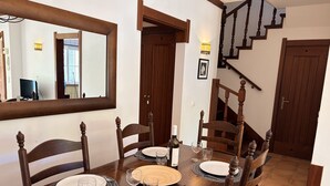 Een eetkamer met een houten tafel gedekt voor vier personen, omringd door stoelen. Een spiegel en een trap zijn zichtbaar op de achtergrond.