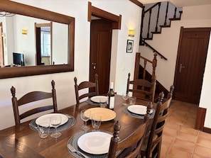 A dining room with a wooden table set for four, surrounded by chairs. A mirror and a staircase are visible in the background. - 28 Terraços de Benagil (Casa Atlantico) (Benagil)