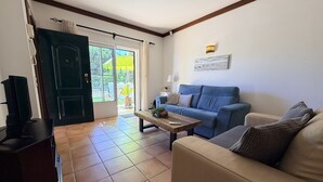 Een woonkamer met een bank, een salontafel, een televisie en een deur naar een balkon.