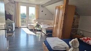 Une chambre avec un lit, un canapé, une armoire en bois, une petite table avec une plante, et un balcon avec vue.