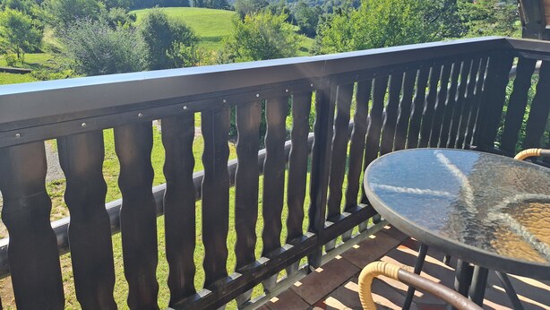 Un balcon donnant sur un paysage verdoyant et une église située au loin.