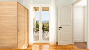 Een kamer met een houten garderobe, een glazen schuifdeur naar een terras buiten met een tafel en stoelen, en een witte deur.