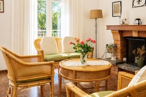 Ein gemütliches Wohnzimmer mit Rattanmöbeln, einem Kamin und Blick auf Grün.