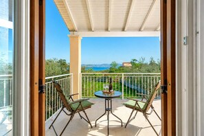 Ein Balkon mit Tisch und Stühlen, Blick aufs Meer und eine gebirgige Landschaft im Hintergrund.