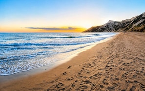 Ein Strand mit Wellen, blauem Himmel und einer felsigen Klippe.