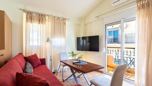 Ein Wohnzimmer mit einer Couch, einem Tisch, einem Fernseher und einem Balkon mit Gartenmöbeln.