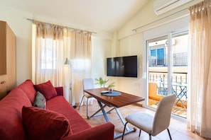 A living room with a sofa, a table, a TV, and a balcony with outdoor furniture. - Modern City-center Studio in the Heart of Kalamata (Kalamata)