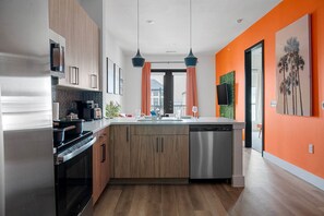A modern kitchen with wooden cabinets, stainless steel appliances, and a large island. - Sapphire Sunset Modern Retreat Near Lake Pool Gym (Rowlett)