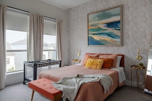 A bedroom with a bed, a crib, a bedside table, a lamp, and a window with curtains. - Sapphire Sunset Modern Retreat Near Lake Pool Gym (Rowlett)