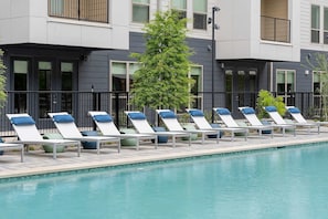 A poolside area with lounge chairs and a tree. - Sapphire Sunset Modern Retreat Near Lake Pool Gym (Rowlett)