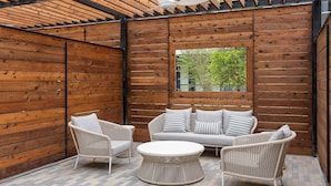 Un espace extérieur aménagé avec un toit, doté d’un mur en bois, d’un canapé, de deux fauteuils et d’une table ronde.