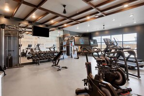 A gym with cardio equipment, weight machines, and a TV screen. - Dallashaus Pool Gym Love Field (Dallas)