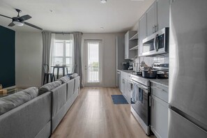 A modern kitchen with stainless steel appliances, a grey sofa, and a ceiling fan. - Dallashaus Pool Gym Love Field (Dallas)
