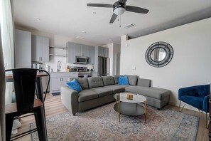 A modern living room with a sectional sofa, a coffee table, and a dining area with a chair. - Dallashaus Pool Gym Love Field (Dallas)