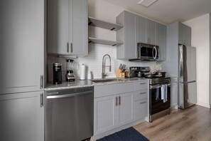 A modern kitchen with grey cabinets, stainless steel appliances, and a microwave above the stove. - Dallashaus Pool Gym Love Field (Dallas)