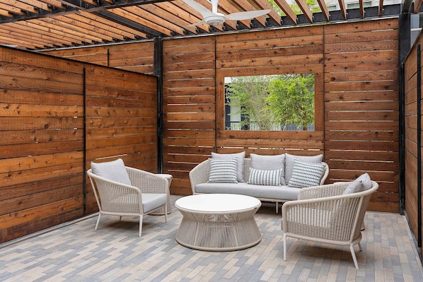 A covered outdoor seating area with a wooden wall, a sofa, two chairs, and a round table. - Sapphire Shores Lakeside Escape Pet Friendly (Rowlett)