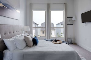 A bedroom with a large bed, a TV, and a window with a view of buildings. - Sapphire Shores Lakeside Escape Pet Friendly (Rowlett)
