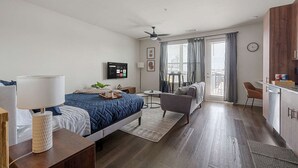 Una habitación de hotel moderna con cama, mesita de noche, lámpara, televisor y un balcón con vistas.