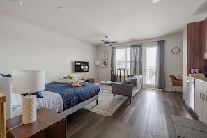 A modern hotel room with a bed, bedside table, lamp, TV, and a balcony with a view. - Dallashaus Pool Gym Love Field (Dallas)