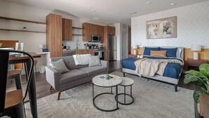 Un apartamento moderno con kitchenette, una sala de estar con sofá y mesita de centro, un dormitorio con cama y mesita de noche, y un ventilador de techo.