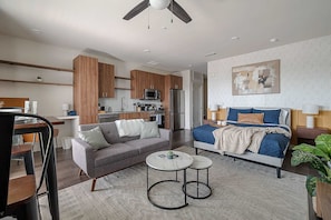 A modern apartment with a kitchenette, a living area with a sofa and coffee table, a bedroom with a bed and nightstand, and a ceiling fan. - Dallashaus Pool Gym Love Field (Dallas)