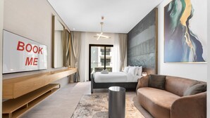 Une chambre d’hôtel moderne équipée d’un lit, d’un canapé, d’une télévision, d’un tableau et d’une grande fenêtre.