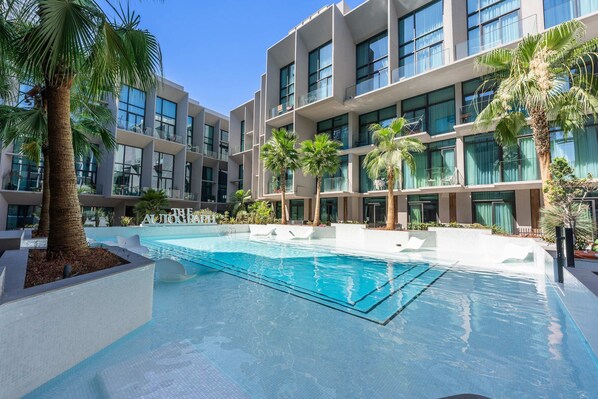 Ein modernes Hotel mit einem zentral gelegenen Schwimmbad, mehreren Balkonen und Palmen.