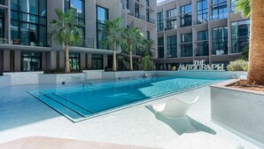 Un bâtiment moderne doté d’une piscine, de palmiers et de l’inscription « THE ALCOGRAP » sur sa façade.