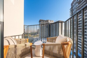 Ein Balkon mit Korbmöbeln, einem kleinen weißen Tisch und Blick auf hohe Gebäude.