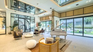 A spacious lobby with a grand piano, comfortable seating, and large windows offering views of the outdoors. - Free Housekeeping Visits During Your Stay - Stayshort - Modern 1 Bedroom in Dubai Hills That Sleeps 4 Great Location (Dubai)