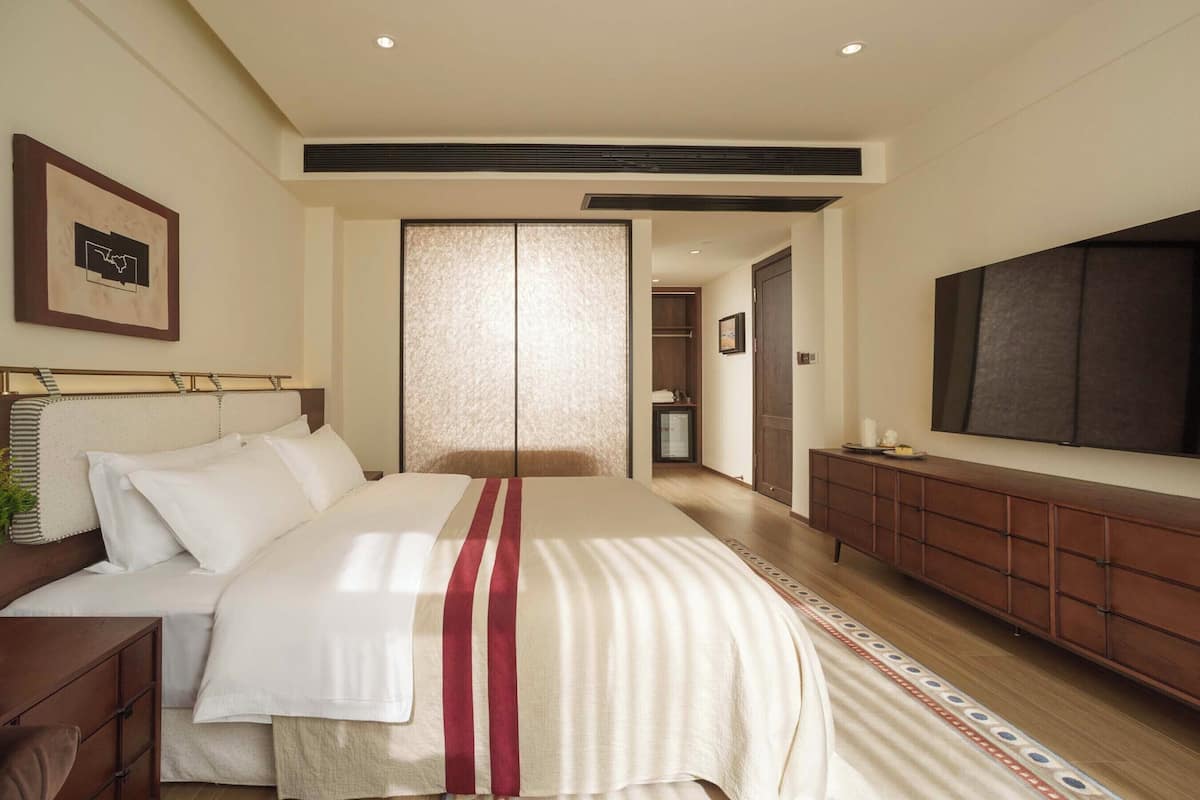 Um quarto com cama, mesa de cabeceira, guarda-roupa e um espelho grande.