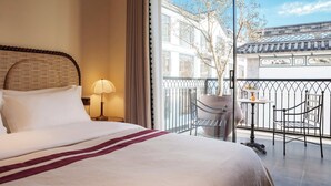 A hotel room with a bed, a nightstand, a lamp, a balcony with chairs, and a view of traditional architecture. - BLOSSOM Floral Art Aesthetic Villa (Dali)