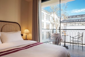 A hotel room with a bed, a nightstand, a lamp, a balcony with chairs, and a view of traditional architecture. - BLOSSOM Floral Art Aesthetic Villa (Dali)
