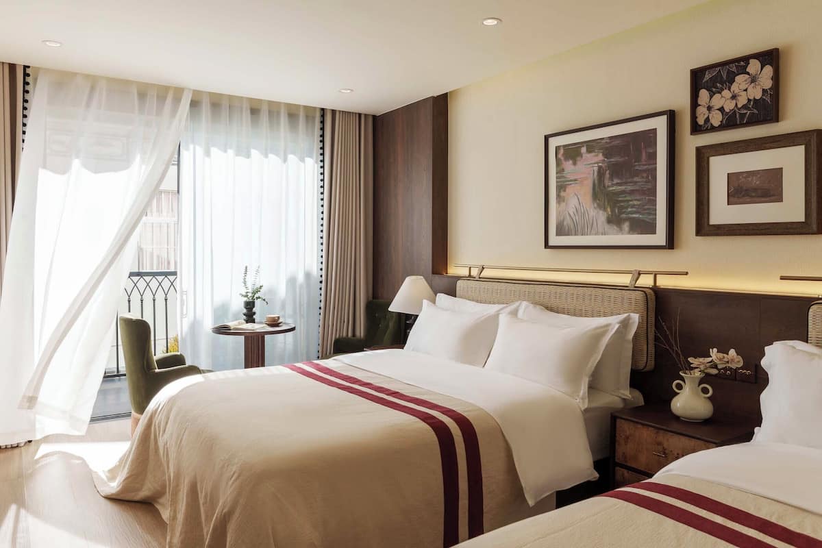 Quarto de hotel com uma cama grande, uma mesa de cabeceira com um vaso, uma cadeira e vista para o exterior.