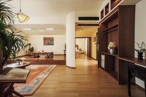 A spacious living area with a wooden floor, a round table, and a sofa. There is a bookshelf with decorative items and a large plant. - BLOSSOM Floral Art Aesthetic Villa (Dali)