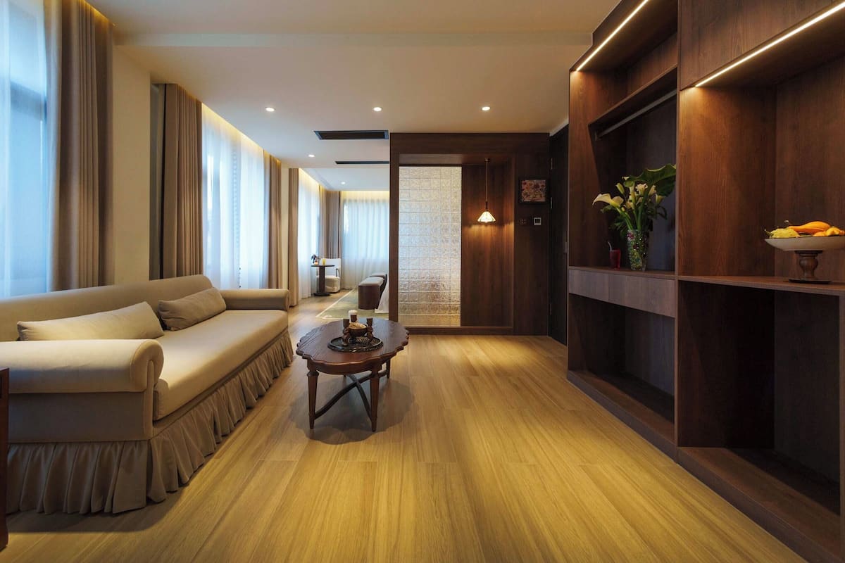 Quarto de hotel moderno com sofá, mesa redonda e prateleira de madeira com um vaso.