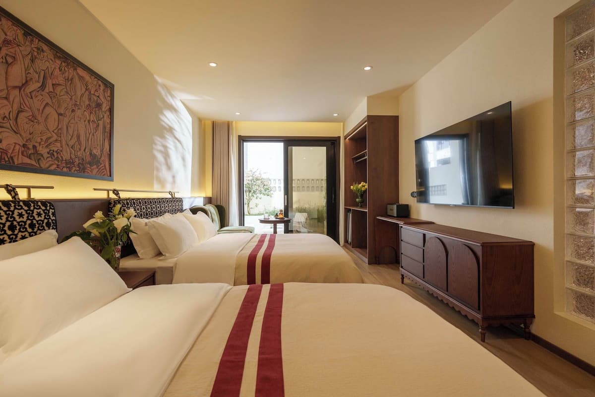 Quarto de hotel com duas camas, televisão, guarda-roupa e um quadro grande na parede.