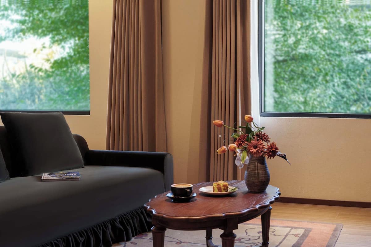 Quarto com sofá, uma pequena mesa com um vaso de flores, um prato com uma fatia de bolo e uma xícara de café.